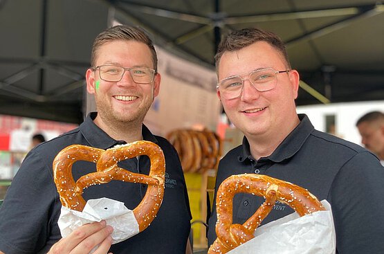 Zwei junge Männer mit großen Brezeln in der Hand bei einem Event